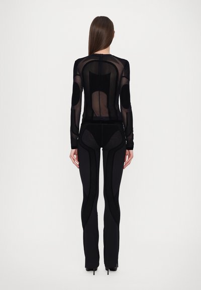 Black sheer long-sleeve top with vertical ribbed texture, paired with fitted black pants featuring ribbed accents and flared hems.