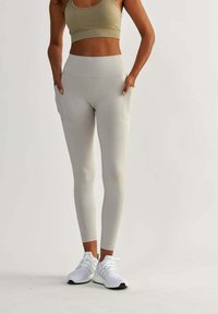 Leggings grigi chiaro con vita alta e tasche laterali. Realizzati in materiale elastico, abbinati a scarpe da ginnastica bianche e un top corto beige.