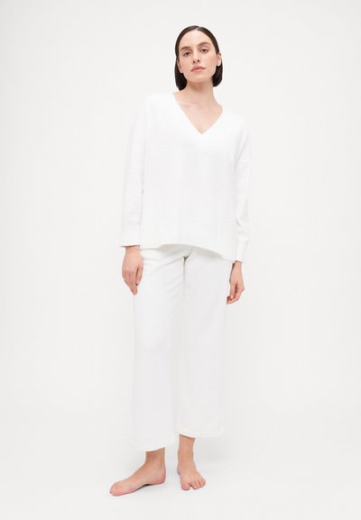 White long-sleeve V-neck sweater with a loose fit, paired with wide-leg white lounge pants featuring rolled hems, both made from soft fabric.