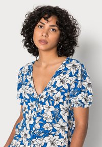 Vestido de mangas curtas e decote em V, feito de tecido azul com padrões florais brancos. Apresenta botões na parte da frente e um acabamento texturizado.