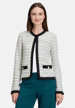 Veste en tweed noire et blanche avec un col rond, des bordures frangées et des poches contrastantes dotées de boutons blancs ; associée à un pantalon teal.