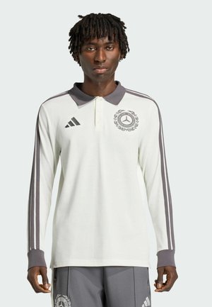 Polo blanco de manga larga con cuello y puños grises. Presenta rayas grises en las mangas y un logotipo en el pecho. Tejido ligero.