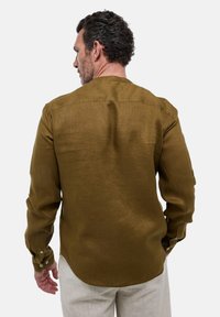 Chemise en lin marron avec un col boutonné, manches longues et fentes sur les côtés ; vue de dos, montrant une texture lisse et un subtil éclat.