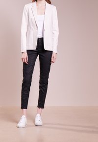 Blazer blanc avec revers crantés, deux poches avant et fermoir à un bouton, associé à un pantalon noir slim-fit et des baskets blanches.