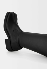 Black leather ankle boot with a chunky platform sole and curved design. Smooth texture with a side seam detail, showcasing a modern silhouette.