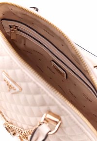 Borsa a tracolla trapuntata color crema con hardware dorato, dotata di tasca interna con zip e logo del marchio stampato sulla fodera beige.