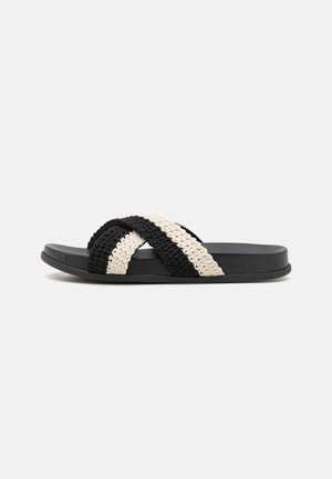 Black and cream woven slide sandal with a flat rubber sole, featuring two crisscrossed braided straps made of soft, textured material.