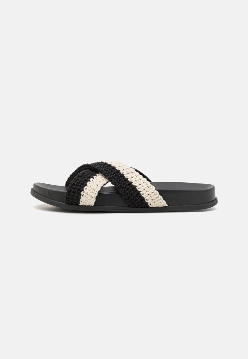 Sandália slide tecida em preto e creme, com sola plana de borracha, apresentando duas tiras trançadas cruzadas feitas de material macio e texturizado.