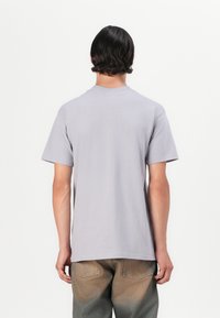 Lys grå bomulds T-shirt med korte ærmer og rund hals, med et enkelt design. Fremhævet med slidte denimjeans.