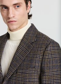 Blazer in tessuto scozzese marrone con accenti blu navy e crema, caratterizzato da un colletto a punta, una morbida texture e un dolcevita a coste crema sovrapposto.
