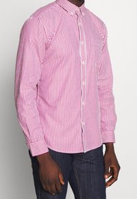 Chemise pour homme à manches longues, rayée rose et blanche, en coton, avec un col boutonné et une poche plaquée sur la poitrine.