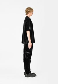Camiseta oversized de pana negra con mangas cortas, combinada con pantalones cargo negros que cuentan con bolsillos y una textura elegante. Calzado negro.