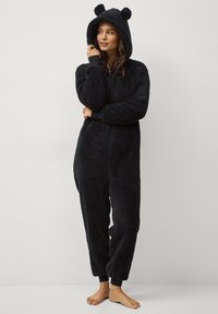 Zwart donzig onesie met een rits aan de voorkant, capuchon met berenoren, ribbewerkte manchetten en een zachte textuur, ontworpen voor comfort en warmte.