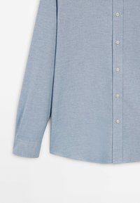 Chemise bleu clair à manches longues avec boutons blancs et une seule manchette, présentée sur fond blanc.