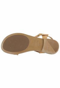 Sohle aus braunem Sandalen mit strukturiertem Gummi, das eine leichte Wölbung, flaches Design und eine minimale Hardware-Akzentuierung in der Nähe des Riemens aufweist.