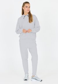 Lichtgrijze hoodie met een trekkoord, gecombineerd met een bijpassende sportbroek. De outfit is gemaakt van zacht materiaal en heeft een losse pasvorm met minimale details.