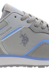 Šedé sportovní tenisky s hladkým syntetickým svrškem a modrými akcenty, kulaté šnúrky a logo jezdec na boku.