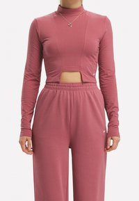 Rosa långärmad tröja med hög hals och utskärning vid midjan, parat med matchande löst sittande byxor. Mjuk, slät tyg.
