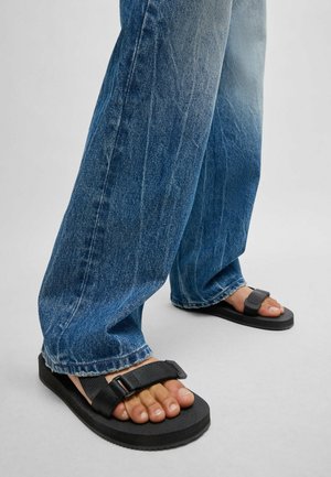 Svarta sandaler med justerbara remmar och tjocka sulor, i kombination med löst sittande blå denimjeans med en blekt design och fransade fållar.