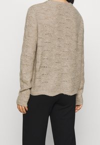 Pull beige en maille avec un motif texturé, coupe décontractée et poignets côtelés. Ourlet festonné et détails en maille ajourée pour une meilleure respirabilité.