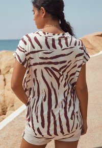 Vit t-shirt med mörkröda zebra ränder, korta ärmar, avslappnad passform och bred halsringning, i kombination med ljusa shorts.