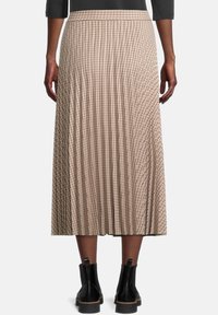Falda midi plisada en beige con un patrón de cuadrícula, con una cinturilla ancha y botas negras hasta el tobillo con acabado texturizado.
