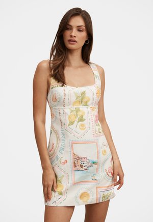 Mujer con un vestido mini sin mangas con estampados coloridos inspirados en la Costa de Amalfi, que incluyen limones, conchas marinas, cerezas e ilustraciones costeras.