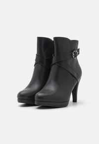 Botines de piel negra hasta el tobillo con punta afilada, tacón alto y detalle de correa cruzada con una hebilla decorativa en el tobillo.