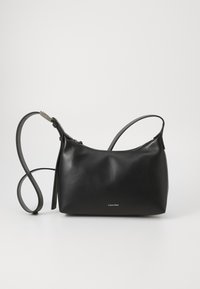 Čierna kožená kabelka s hladkou text�úrou, minimalistickým dizajnom, zipsom a nastaviteľným popruhom. Obsahuje jemné logo Calvin Klein.