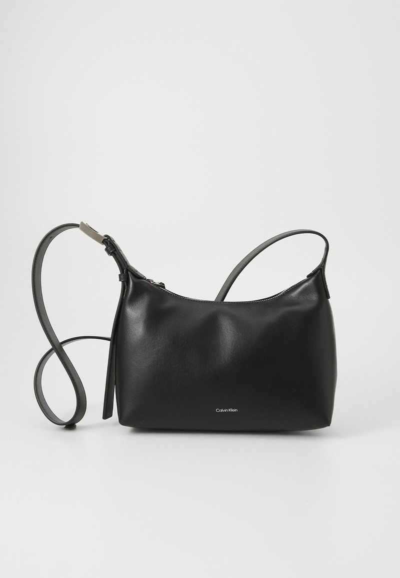 Sorte læderhåndtaske med en glat tekstur, minimalistisk design, lynlåslukning og justerbar rem. Har diskret Calvin Klein branding.