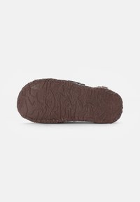 Brown rubber sole with textured surface and wavy pattern; features a small brand label on the side.