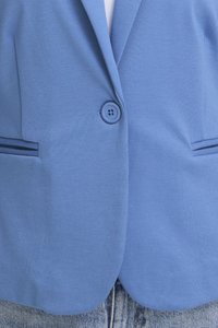 Hellblauer Blazer mit Ein-Knopf-Verschluss und Schlitztaschen, getragen über einem weißen Oberteil und kombiniert mit hellen Jeans.