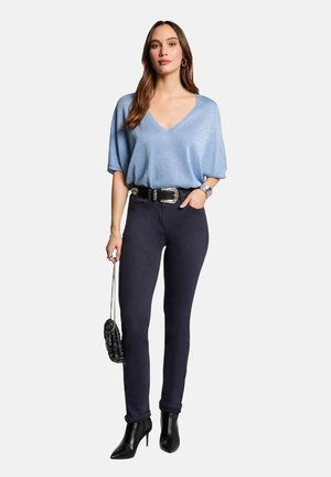 Top V-nella a maniche corte di colore azzurro chiaro, abbinato a jeans skinny scuri, una cintura nera e décolleté neri a punta; tiene una borsetta piccola.