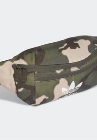 Kamikaze-mönstrad midjeväska med två mörkgröna dragkedjor och en vit Adidas trefoil-logotyp på framfickan.