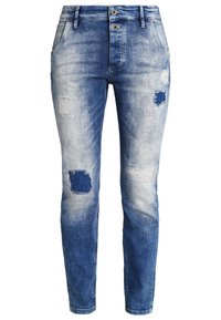 Vaqueros de mezclilla azul claro con detalles desgastados, incluyendo parches y desgastes. Cuenta con cierre de botón y cremallera, diseño de cinco bolsillos.