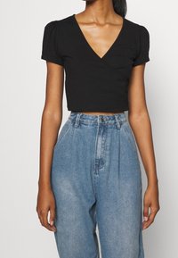 Hauts courts à manches courtes en noir avec un décolleté en V, fabriqué dans un tissu doux ; associé à un jean en denim bleu clair taille haute.