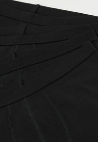 Schwarze Baumwollunterwäsche mit glatter Textur, ausgestattet mit einem genähten Bund und Nähten. Mehrere Paare übereinander gestapelt.