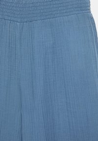 Plave hlače od teksturiranog tkanja s širokim elastičnim pojasom i okomitim rebrastim uzorkom.