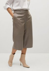 Culottes in ecopelle beige con vita alta, tasche laterali e texture liscia. Abbinati a stivaletti beige con tacco alto.