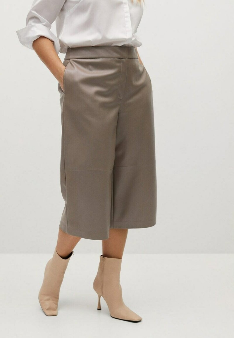 Culottes in ecopelle beige con vita alta, tasche laterali e texture liscia. Abbinati a stivaletti beige con tacco alto.