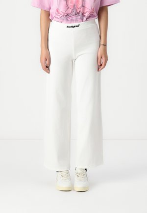 Wide-leg white pants made from a textured fabric, featuring a black waistband with "lowlights" branding. Paired with white sneakers.