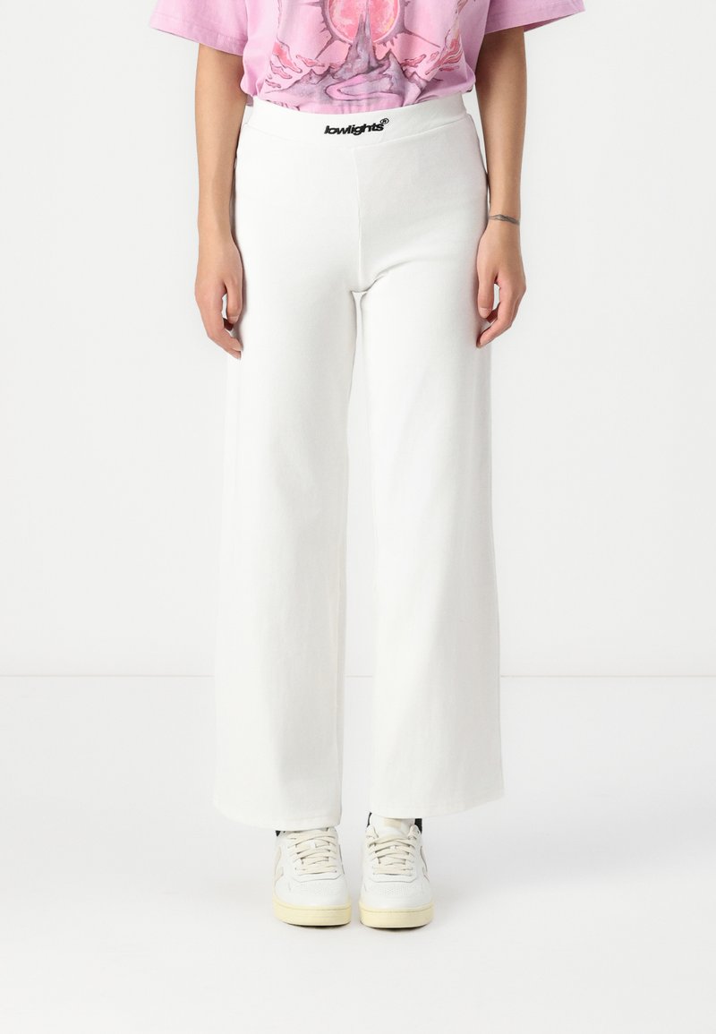 Wide-leg white pants made from a textured fabric, featuring a black waistband with "lowlights" branding. Paired with white sneakers.