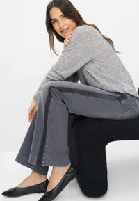 Grå jeans med bred ben-design, der har en sort sidestribe og tekstureret finish. Kombineret med en lys grå, pailetteret sweater og flade sko.