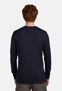 Laivastonsininen pitkähihainen paita, joka on valmistettu pehmeästä materiaalista. Siinä on pyöreä pääntie, slim fit -silhuetti ja sileä rakenne, sekä ommellut saumat.