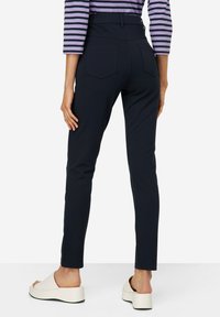 Granatowe spodnie slim-fit o wysokim stanie, z dwoma tylnymi kieszeniami i gładką fakturą, w połączeniu z białymi butami na platformie.