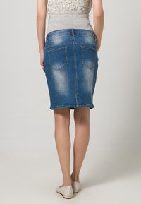 Džínová tužková sukně ve vybledlé modré barvě, s zadními kapsami, přiléhavým střihem a lemem, který končí těsně nad koleny.