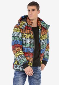 Kleurrijke pufferjack met een mix van bold letters in blauw, groen, rood en geel op een zwarte achtergrond; inclusief een capuchon en geribbelde manchetten.