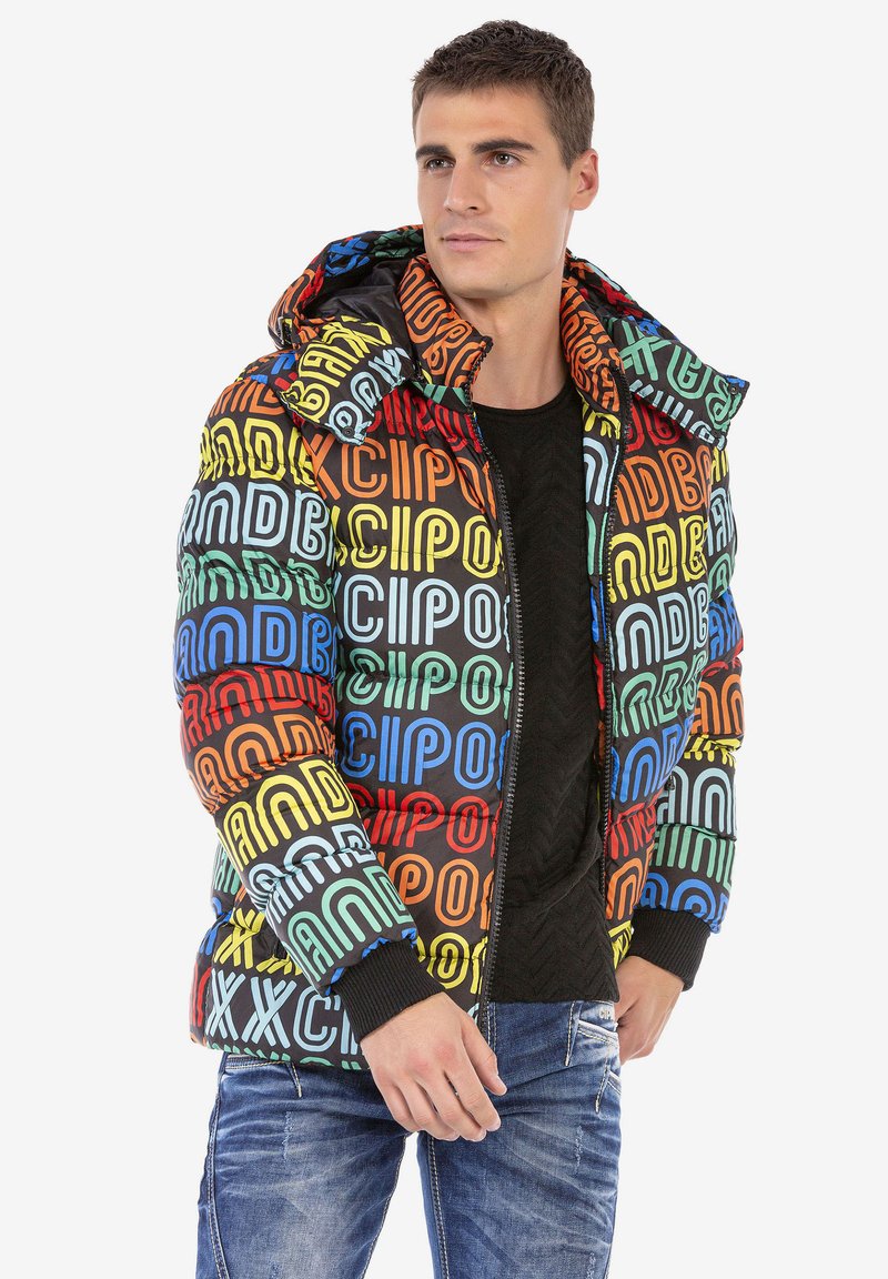 Kleurrijke pufferjack met een mix van bold letters in blauw, groen, rood en geel op een zwarte achtergrond; inclusief een capuchon en geribbelde manchetten.