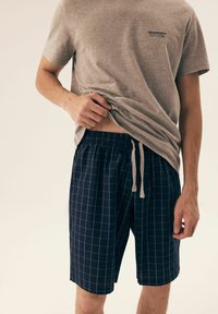 Szara bawełniana koszulka z krótkim rękawem, zestawiona z niebieskimi szortami w kratę, posiadającymi elastyczny pasek w talii i regulowany sznurek.