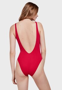 Bañador rojo de una sola pieza con un diseño de espalda en V profunda, tirantes finos y una silueta ajustada, elaborado en tela texturizada.